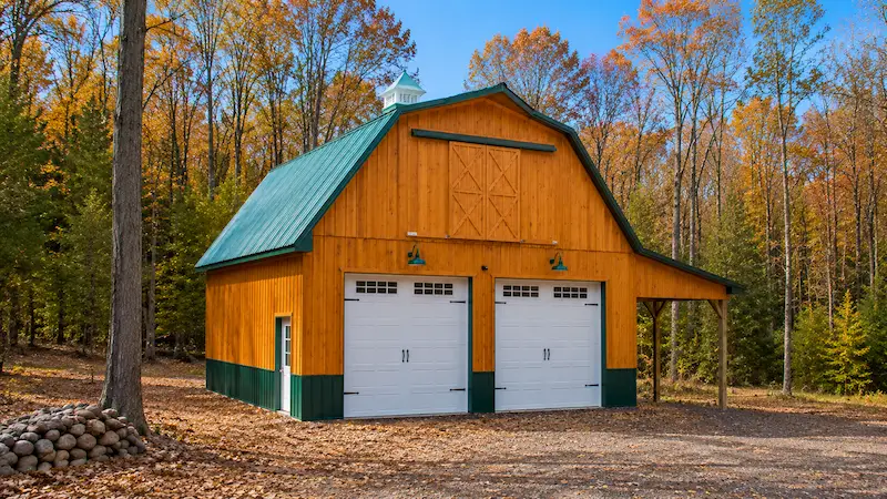 28x30 Pennsylvania pole garage for vehicle storage with board & baton siding, evergreen roof and trim, open sided lean-to, carriage style garage doors, wooden sliding door, and cupola with weathervane