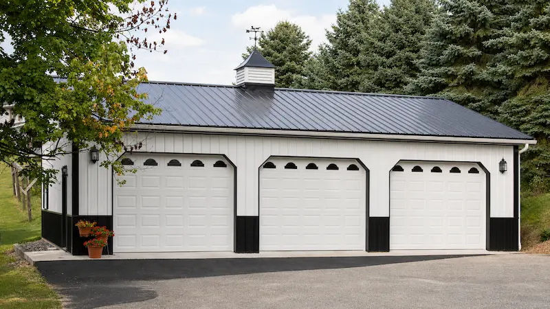 30x40 white pole barn with black roof and trim, three garage doors with windows, shutters, cupola, and wainscoting