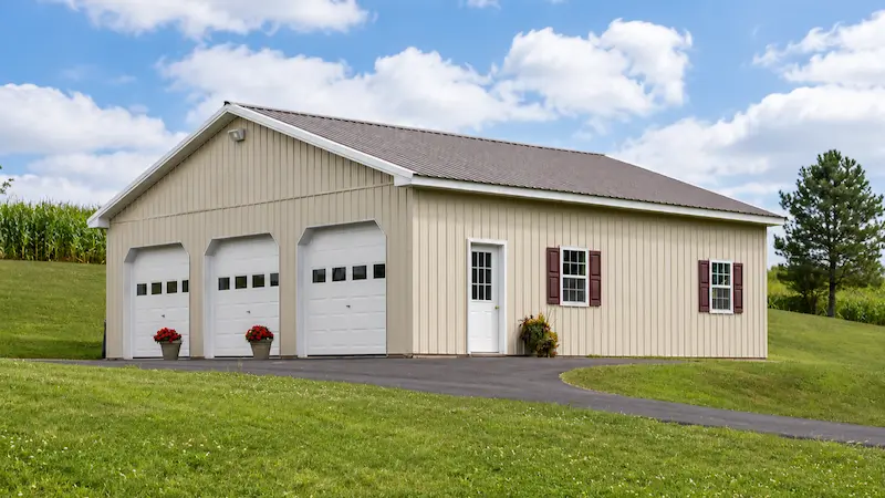 36x36 light stone pole barn with bronze roof, white trim, three garage doors with windows, entry door, and shutters