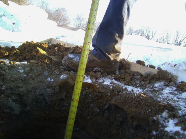 Timberline crew measuring post-hole depth in frozen ground before setting posts for a winter pole-barn project.