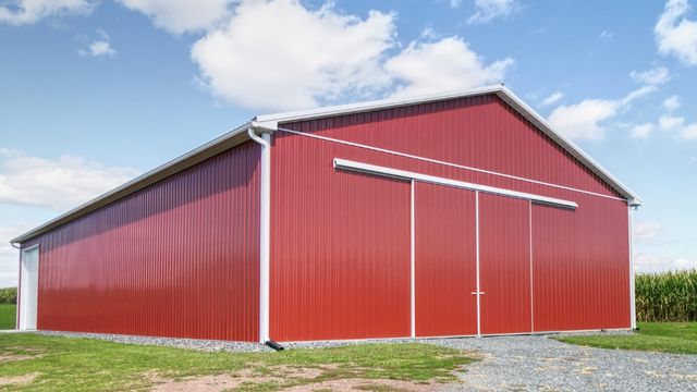 Red agricultural pole building with metal siding and sliding doors for farm storage and equipment use