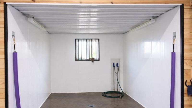 Wash stall with concrete floor and tie rings inside equine barn