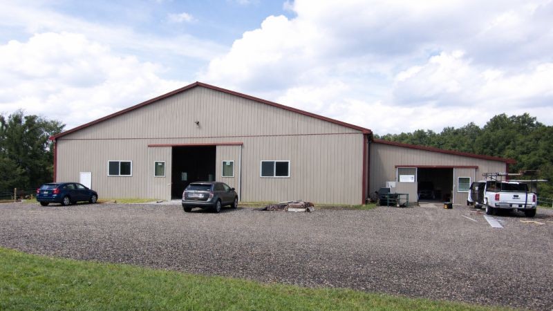 Large indoor riding arena pole barn with red roof and lean-to stall barn