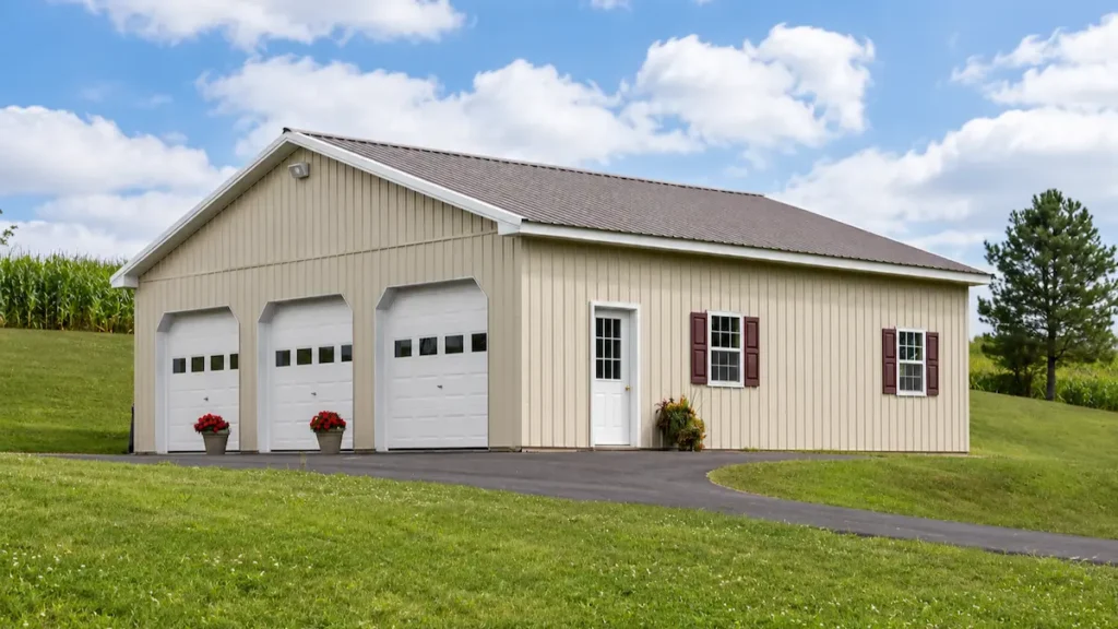 36x36 light stone pole barn with bronze roof, white trim, three garage doors with windows, entry door, and shutters