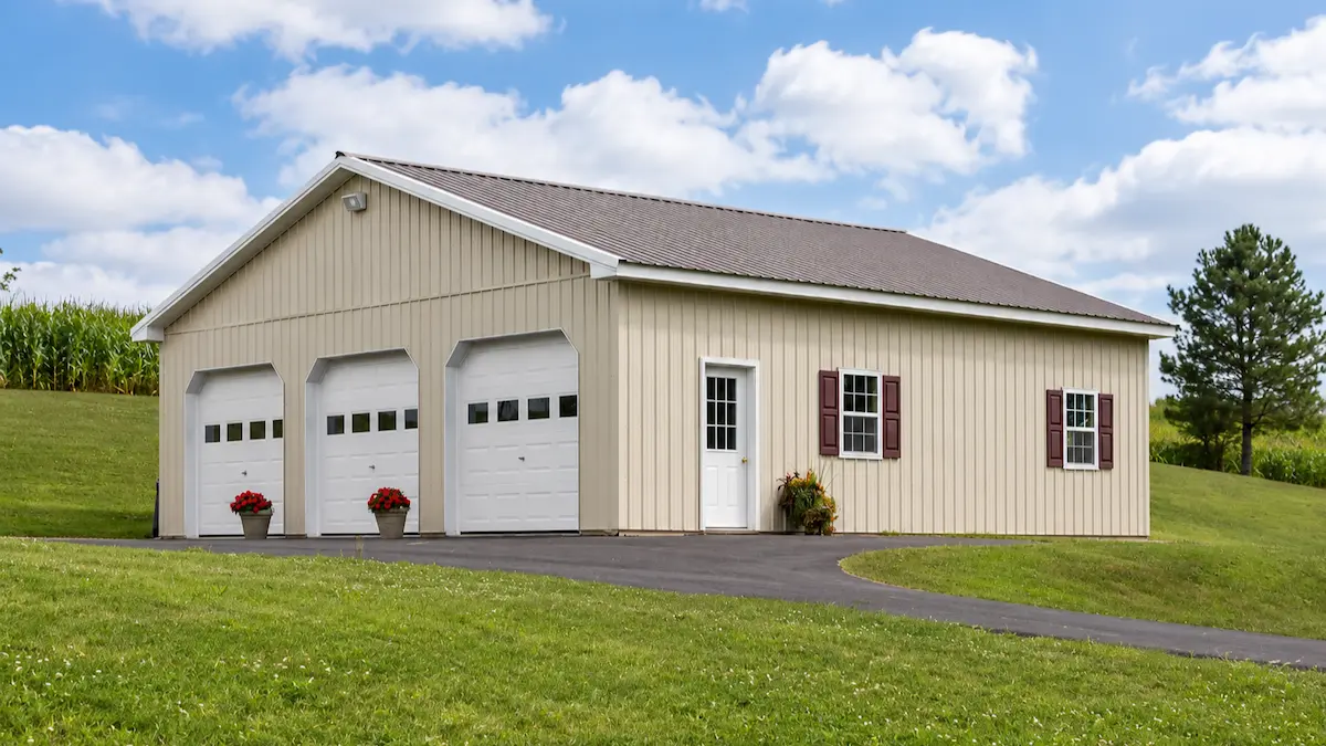 36x36 light stone pole barn with bronze roof, white trim, three garage doors with windows, entry door, and shutters