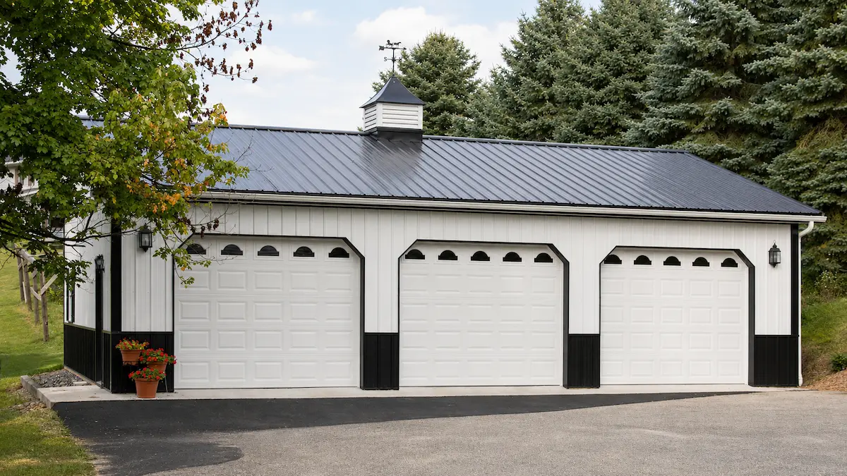 30x40 white pole barn with black roof and trim, three garage doors with windows, shutters, cupola, and wainscoting