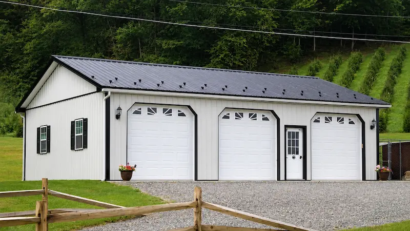 30x40 bone white pole barn with black roof and trim, three garage doors with windows, shutters, snow guards, and gutters