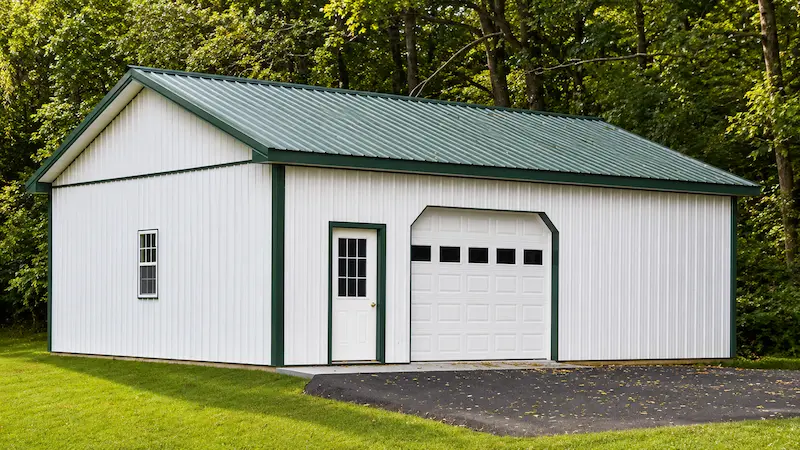 30x32 white pole barn with evergreen roof and trim, garage door with windows, entry door, and single hung window