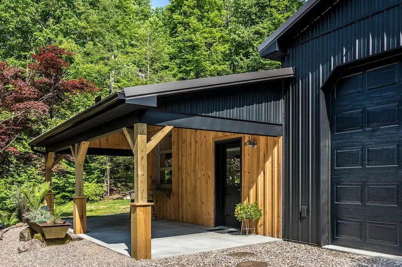 Custom post-frame building with black metal siding, insulated overhead door, and covered timber porch in Pennsylvania